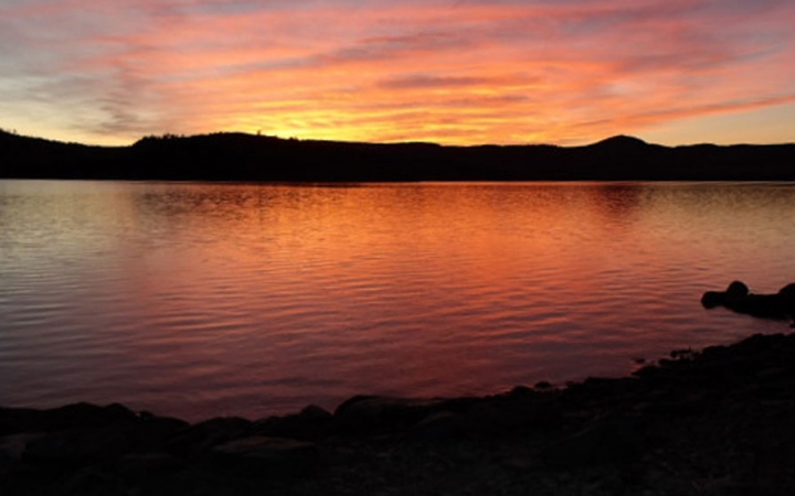 The sky appears in shades of red, orange and purple, and is reflected in the lake below. 